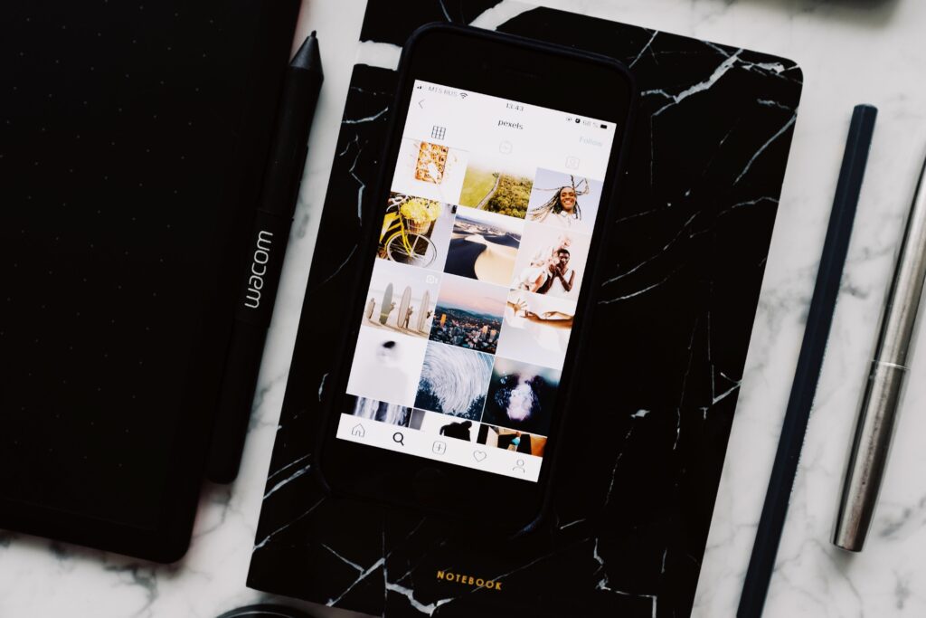 Phone showing a social media photo grid on a dark marble surface